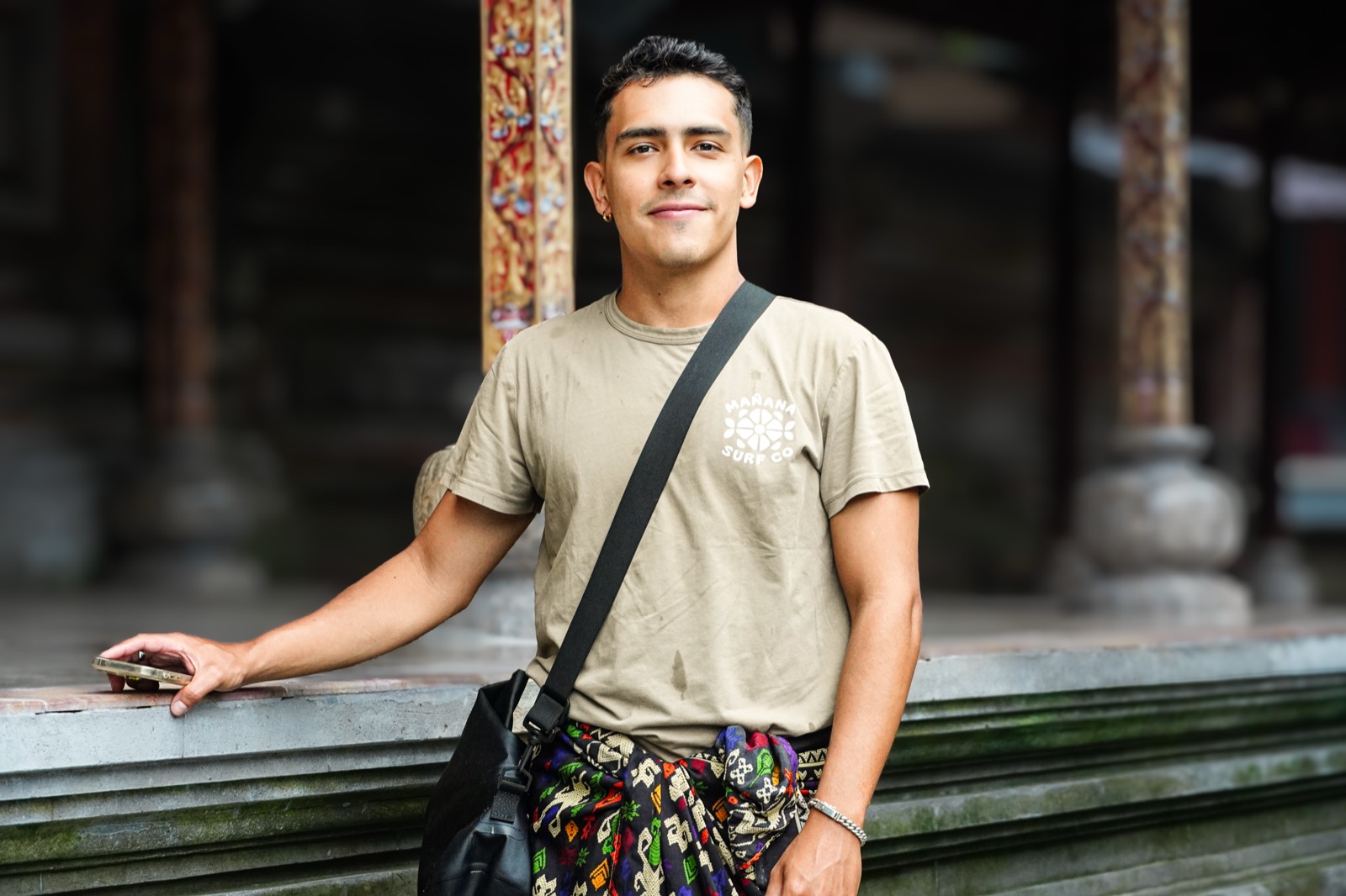 Christian Lozano leaning on a stone ledge in a temple courtyard, smiling